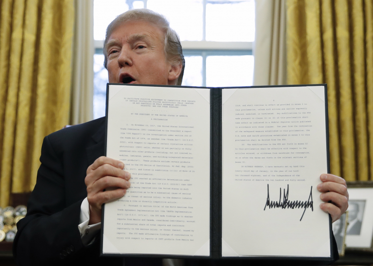 President Donald Trump holds up one of the Section 201 actions that he signed during a ceremony in the Oval Office of the White House in Washington, Tuesday, Jan. 23, 2018. Trump says he is imposing new tariffs to AP